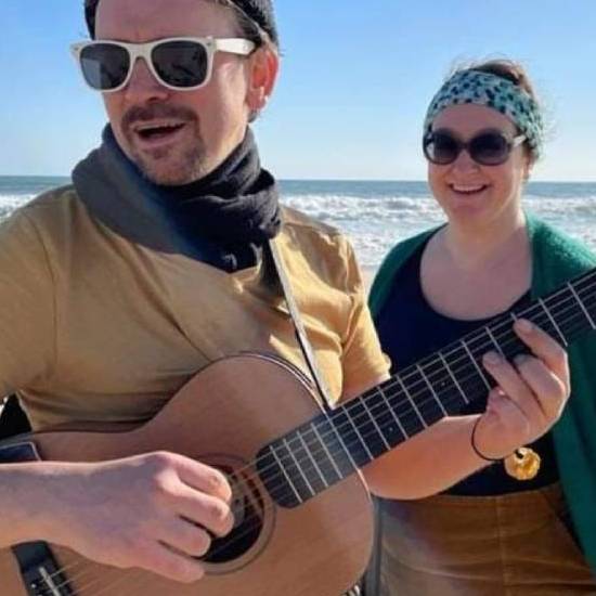 ein Mann mit Gitarre und eine Frau am Strand vor dem Meer