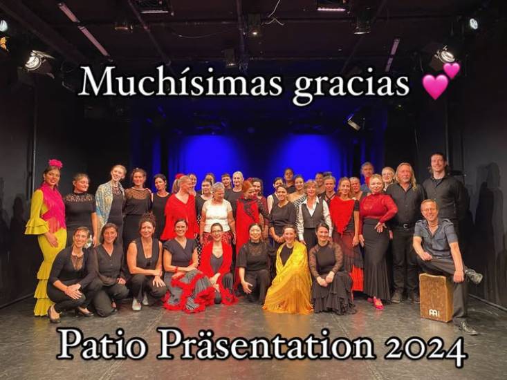 Gruppenfoto einer großen Flamenco-Ensemble-Präsentation 2024: Über 30 Tänzerinnen und Tänzer in bunten Kostümen – Rot, Schwarz, Gelb und Weiß – posieren gemeinsam auf einer Bühne vor blau beleuchtetem Hintergrund. Oben steht der Schriftzug ‚Muchísimas gracias 💕‘, unten ‚Patio Präsentation 2024‘.