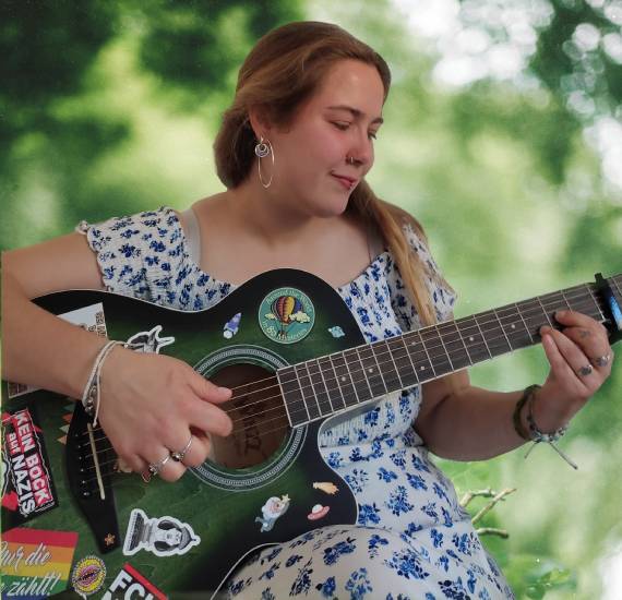 Frau sitzt auf einem Stuhl und spielt Gitarre.
