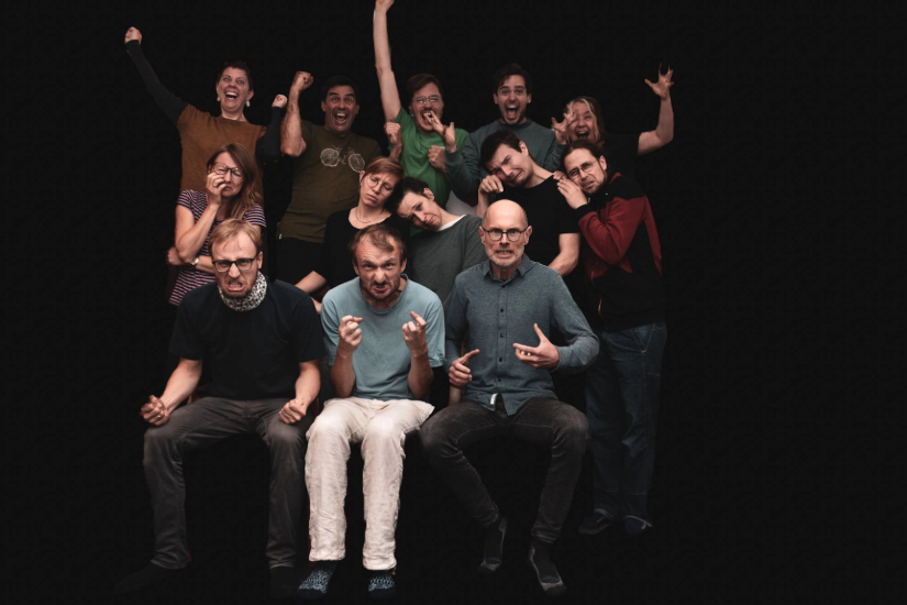 Eine Improtheatergruppe mit 12 Frauen und Männern schaut in die Kamera und zieht Grimassen.
