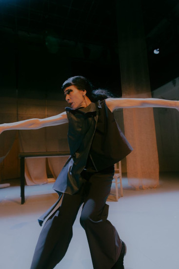 Eine Schauspielerin steht auf einer Bühne in warmem Licht und performt mit weit ausgebreiteten Armen einen ausdrucksstarken Tanz.