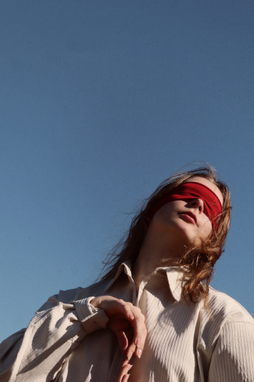 Teilaufnahme einer Frau mit roter Augenbinde, die vor blauem Himmel in Wabi-Sabi-Stil tanzt.