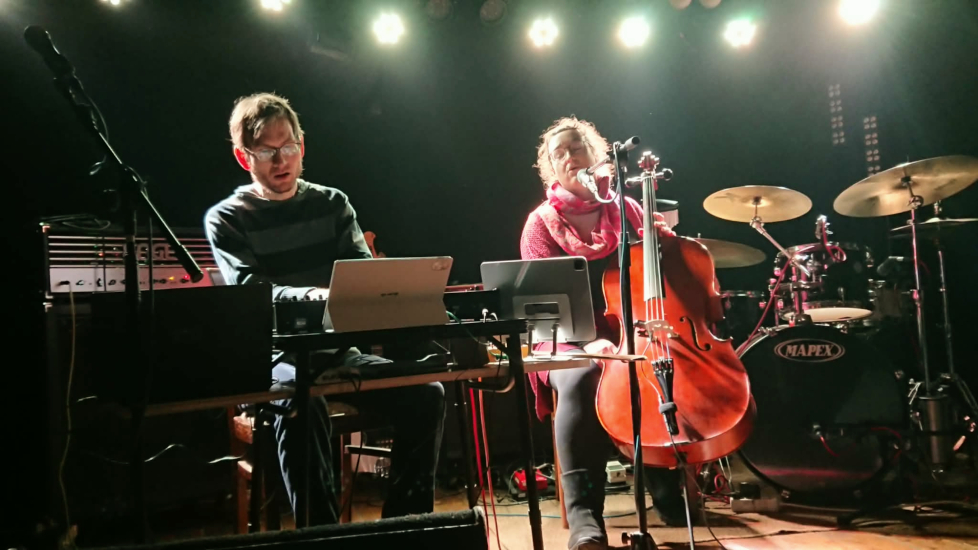Eine Cellistin und ein Mann am Keyboard performen auf einer Bühne.