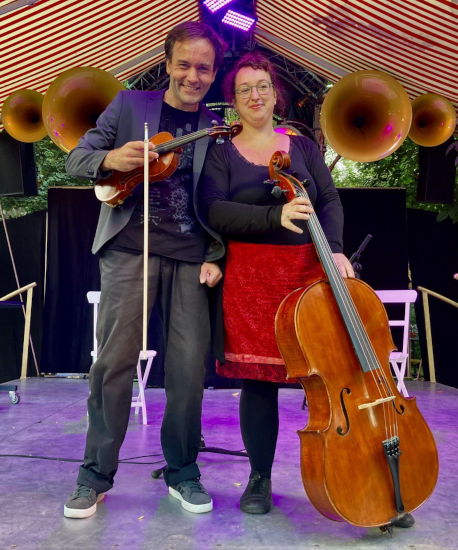 Ein Violinist und eine Cellistin stehen nebeneinander mit ihren Instrumenten auf einer Bühne.