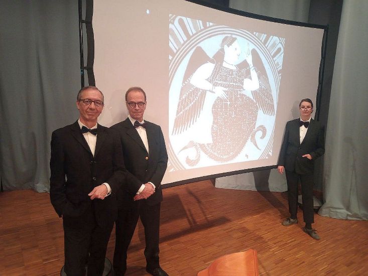 Drei Personen in Anzug stehen neben einer Leinwand. Auf der Leinwand ist ein Bild von Eris, der Göttin des Zweifels