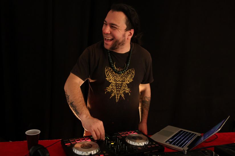 Foto vor einem Mann. Er benutzt ein DJ-Conroller. daneben steht ein Laptop. Er blickt zur Seite und lacht.